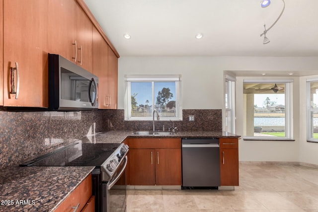 kitchen featuring rail lighting, sink, tasteful backsplash, dark stone countertops, and appliances with stainless steel finishes