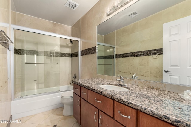 full bathroom featuring shower / bath combination with glass door, tile patterned floors, toilet, and tile walls