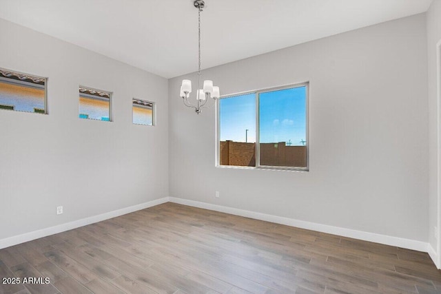 empty room with a notable chandelier, baseboards, and wood finished floors