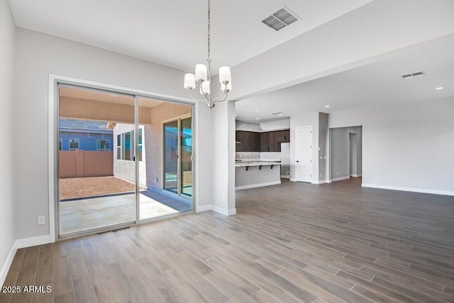 unfurnished room featuring an inviting chandelier, wood finished floors, visible vents, and baseboards