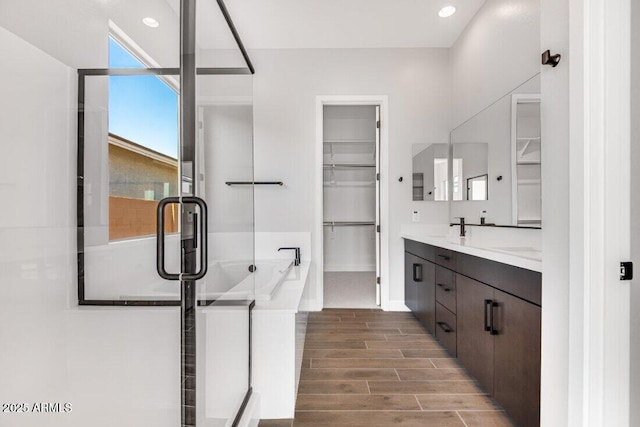 full bathroom featuring vanity, a walk in closet, a garden tub, and wood finish floors