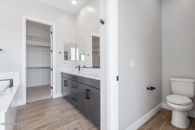 bathroom featuring a walk in closet, toilet, baseboards, and wood finish floors