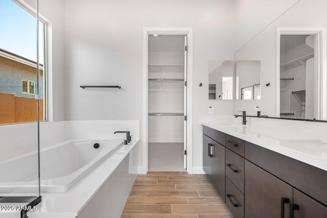 full bath featuring a bath, a walk in closet, wood finish floors, and a sink