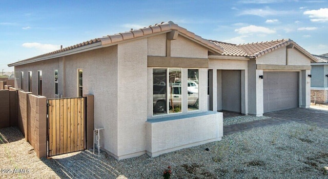 view of property exterior featuring a gate, fence, an attached garage, stucco siding, and a tile roof