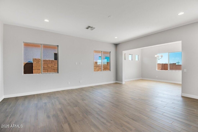 empty room with visible vents, wood finished floors, recessed lighting, an inviting chandelier, and baseboards