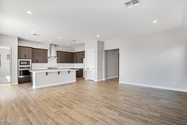 kitchen with oven, visible vents, open floor plan, and wall chimney exhaust hood