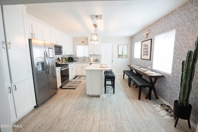 kitchen featuring a kitchen bar, a center island, stainless steel appliances, white cabinetry, and light wood-type flooring