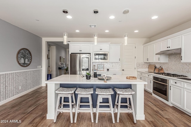 kitchen with white cabinets, appliances with stainless steel finishes, a kitchen island with sink, and pendant lighting