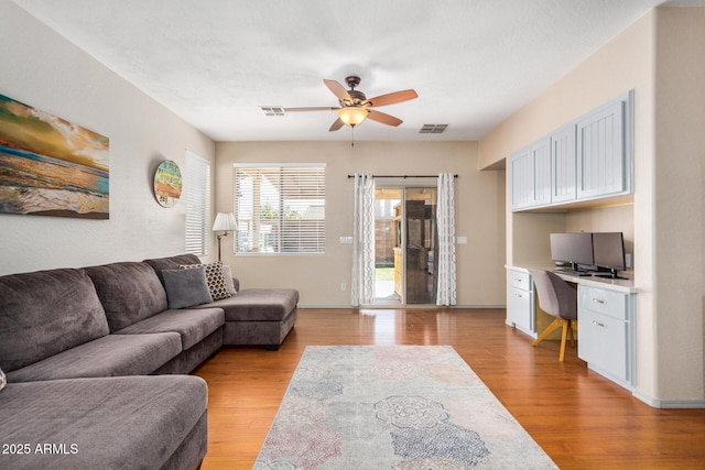 living room featuring built in desk, ceiling fan, and light hardwood / wood-style flooring