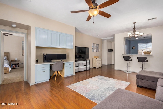 living room with built in desk, ceiling fan with notable chandelier, and dark hardwood / wood-style flooring