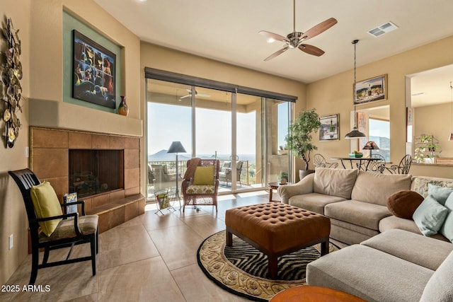 living room featuring a tile fireplace, light tile patterned floors, and ceiling fan