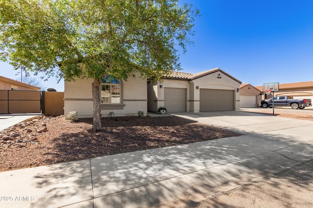 view of front of home featuring a tile roof, stucco siding, driveway, an attached garage, and a gate