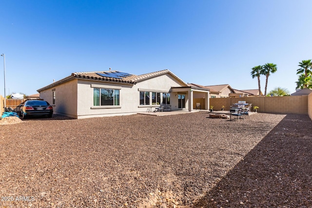 rear view of house featuring stucco siding, a patio, roof mounted solar panels, a fenced backyard, and a tiled roof