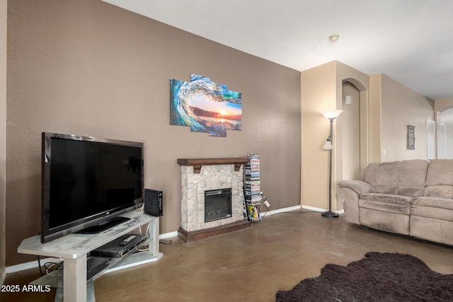 living area featuring arched walkways, concrete floors, a stone fireplace, and baseboards