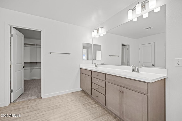 bathroom with a walk in closet, wood finished floors, a sink, and double vanity