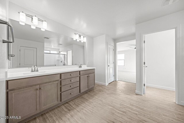 bathroom featuring wood finished floors, a sink, visible vents, baseboards, and double vanity