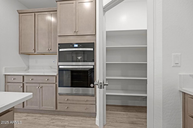 kitchen with a textured wall, light wood finished floors, stainless steel double oven, and light brown cabinetry