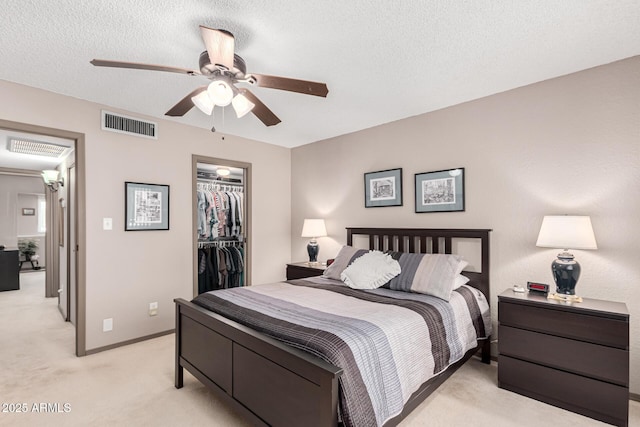 bedroom with light carpet, a textured ceiling, ceiling fan, a spacious closet, and a closet