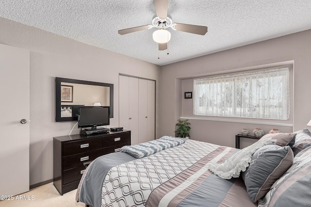 bedroom with a textured ceiling, light colored carpet, a closet, and ceiling fan