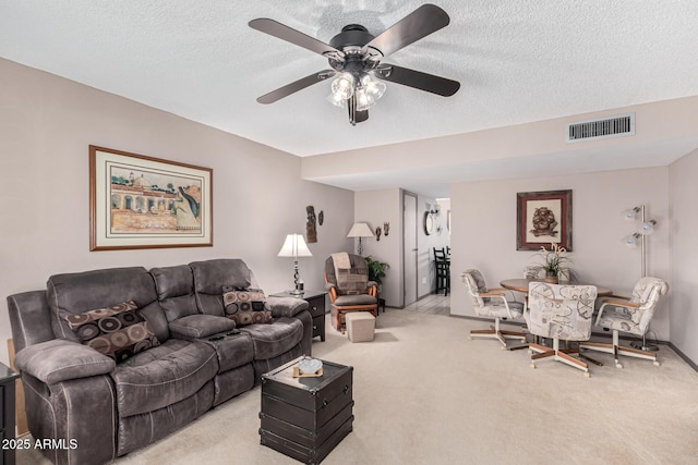 living room featuring ceiling fan, light carpet, and a textured ceiling