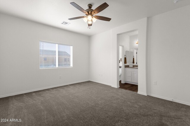 unfurnished bedroom featuring ensuite bath, dark carpet, and ceiling fan