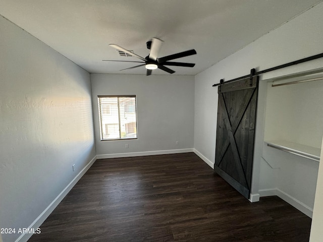 empty room featuring a barn door, dark hardwood / wood-style floors, and ceiling fan