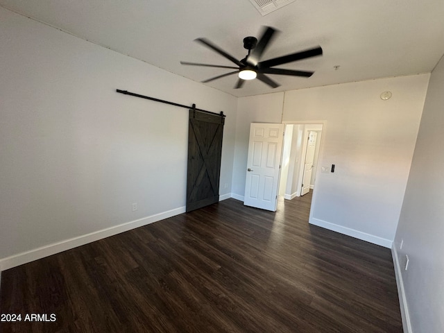 unfurnished bedroom with ceiling fan, a barn door, and dark hardwood / wood-style flooring