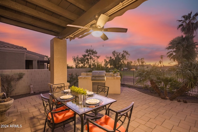 patio terrace at dusk with grilling area, an outdoor kitchen, and ceiling fan