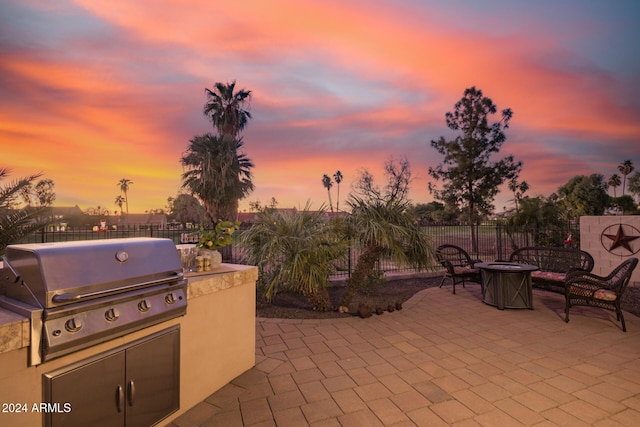 patio terrace at dusk with a grill, a fire pit, and exterior kitchen