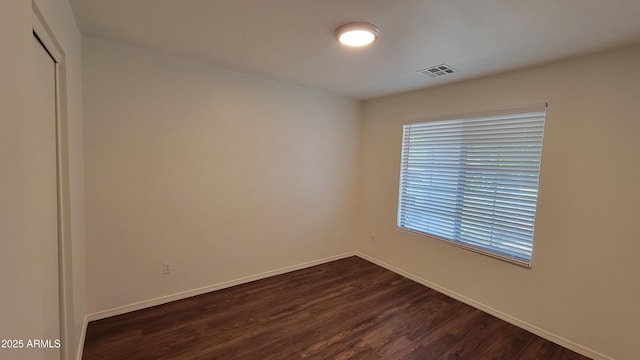 unfurnished room featuring dark wood-style flooring, baseboards, and visible vents