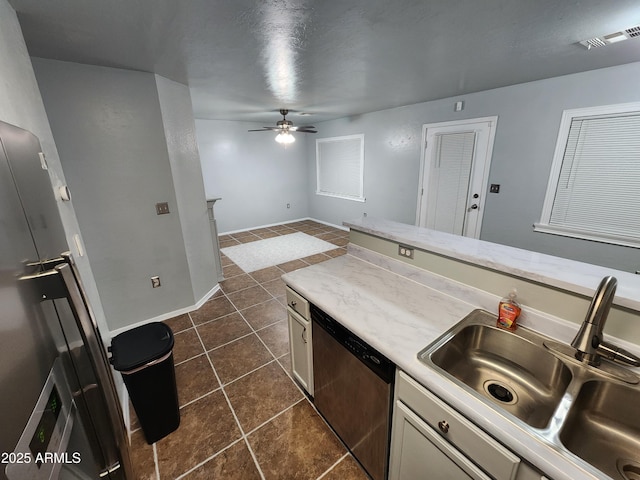 kitchen with stainless steel dishwasher, a ceiling fan, light countertops, dark tile patterned flooring, and a sink