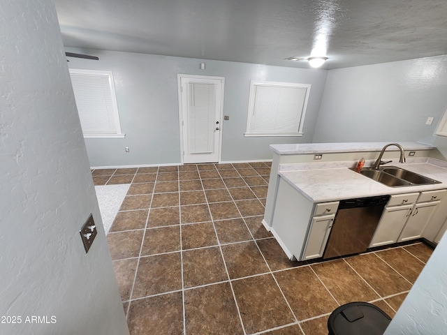 kitchen with a sink, light countertops, dark tile patterned flooring, and stainless steel dishwasher