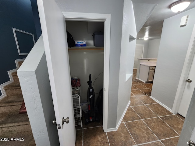 hallway with dark tile patterned flooring, baseboards, and stairs