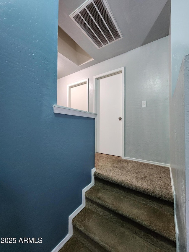 stairs with carpet flooring, a textured wall, and visible vents