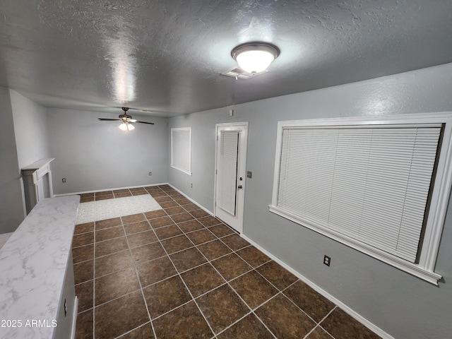 interior space with baseboards, a ceiling fan, a textured ceiling, and dark tile patterned flooring