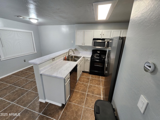 kitchen with a sink, dark tile patterned flooring, white cabinets, a peninsula, and stainless steel appliances