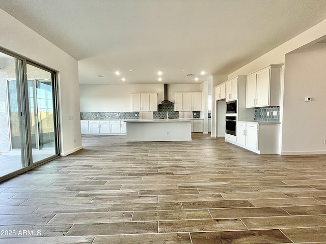 kitchen featuring stainless steel appliances, a kitchen island with sink, wall chimney range hood, and white cabinets