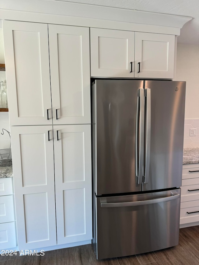 kitchen featuring dark wood-type flooring, light stone countertops, stainless steel refrigerator, and white cabinetry