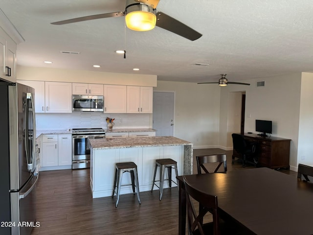 kitchen with a kitchen island, white cabinetry, stainless steel appliances, dark hardwood / wood-style floors, and a breakfast bar area