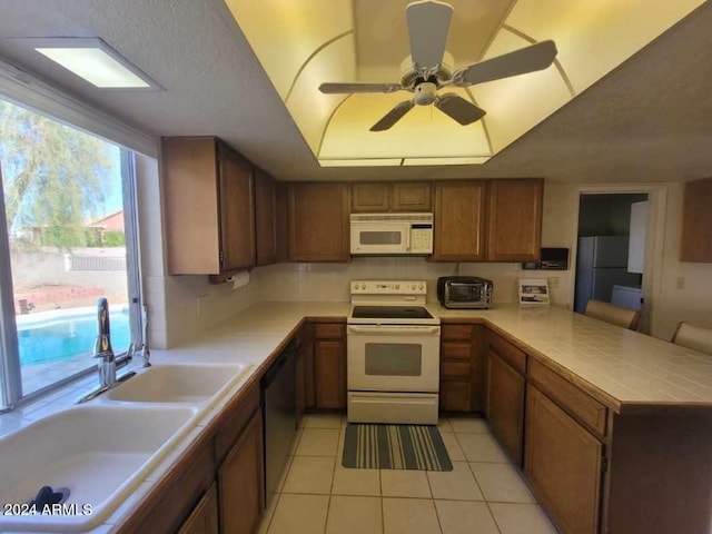 kitchen featuring kitchen peninsula, white appliances, ceiling fan, sink, and light tile patterned floors