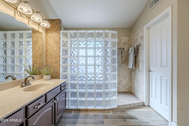 bathroom with hardwood / wood-style flooring, vanity, and a tile shower