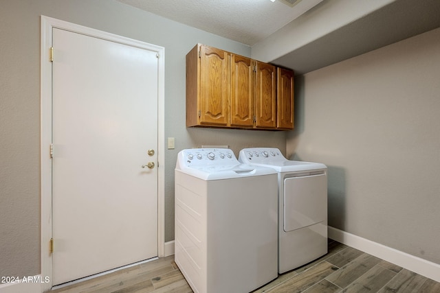 washroom featuring cabinets, washer and clothes dryer, light hardwood / wood-style floors, and a textured ceiling