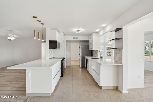 kitchen featuring electric range, sink, stainless steel fridge, decorative light fixtures, and white cabinets