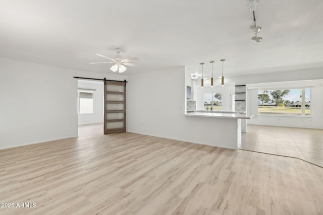 unfurnished living room with ceiling fan, sink, a barn door, track lighting, and light wood-type flooring