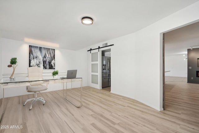 office with a barn door and light hardwood / wood-style flooring