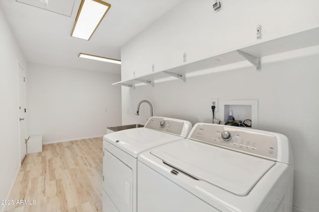 laundry area with light hardwood / wood-style flooring, washer and dryer, and sink