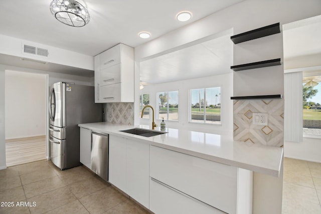 kitchen with appliances with stainless steel finishes, tasteful backsplash, sink, light tile patterned floors, and white cabinetry