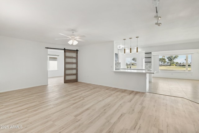 unfurnished living room with a barn door, a wealth of natural light, ceiling fan, and light hardwood / wood-style floors