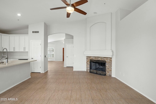 unfurnished living room with visible vents, a ceiling fan, a sink, a stone fireplace, and lofted ceiling