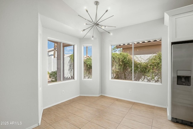 spare room featuring a wealth of natural light, baseboards, and an inviting chandelier